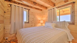 Ein Schlafzimmer einer Holzhütte mit Bett, Vorhängen, einem Fenster und einer Lampe.