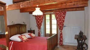 Ein Schlafzimmer mit einem Holzbett, einem Nachttisch, einer Vintage-Nähmaschine und einem Fenster mit floralem Vorhang.