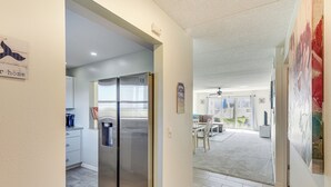 A modern kitchen with stainless steel appliances, a dining area with a table and chairs, and a living space with a large painting. - Coastal Condo Escape: Steps to Beach (Ormond Beach)