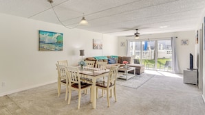 A spacious living area with a dining table and chairs, a sofa, and a balcony with a view. - Coastal Condo Escape: Steps to Beach (Ormond Beach)