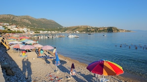 Una playa con sombrillas, barcos y montañas al fondo.