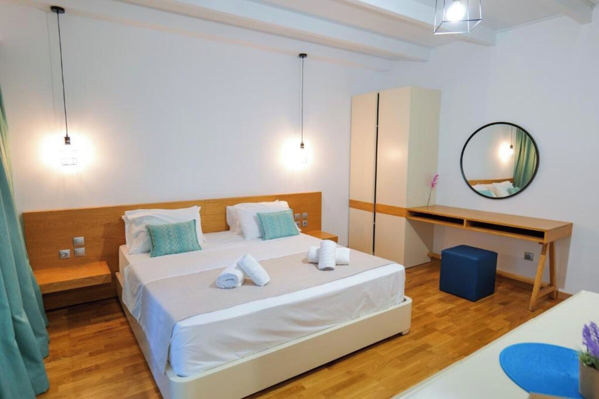 A modern hotel room with a wooden bed, a desk, a mirror, and a blue ottoman.