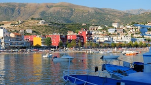 Un pueblo costero con barcos amarrados a lo largo del muelle, edificios al fondo y un paisaje montañoso.