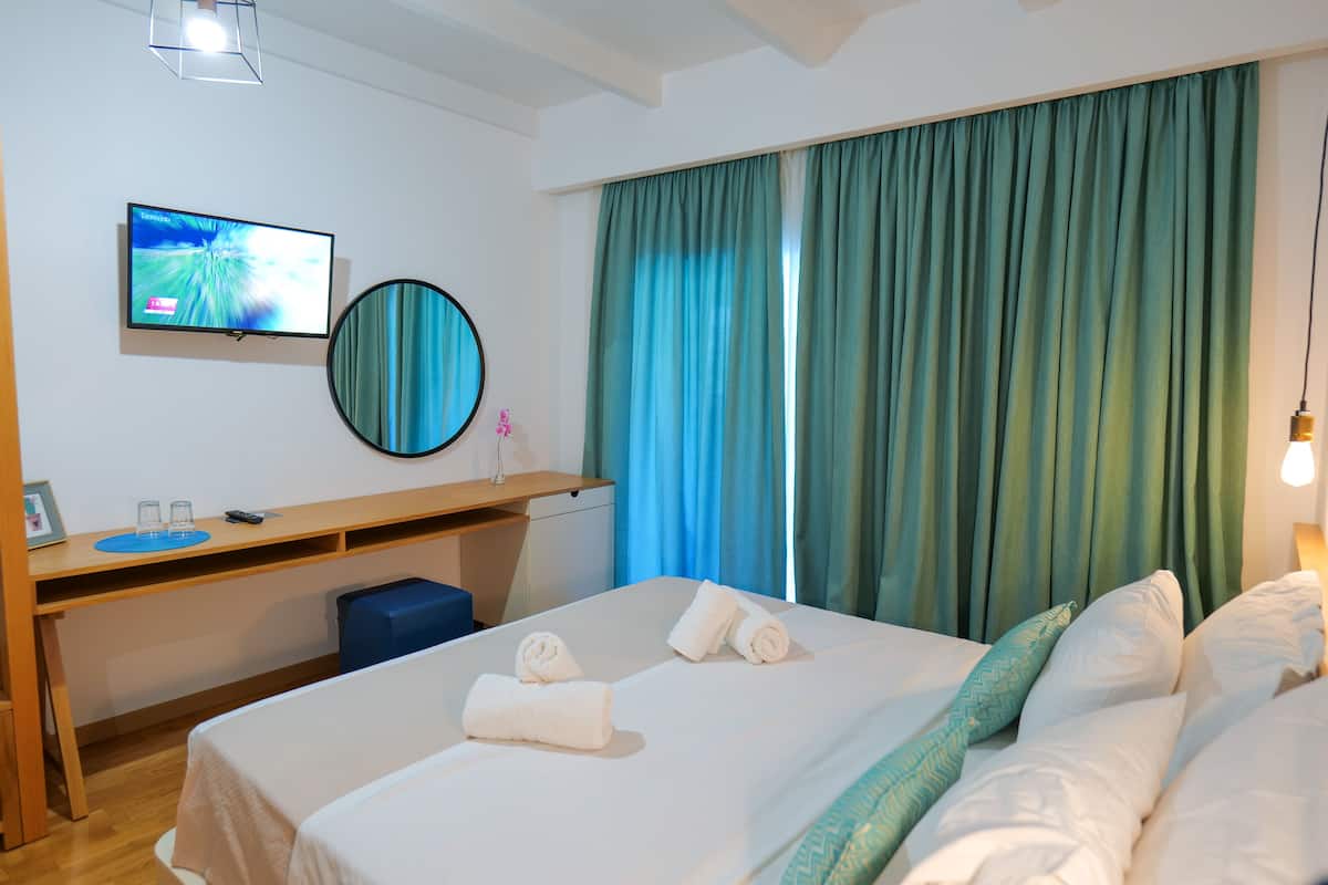 A hotel room with a bed, a desk, a TV, a mirror, and curtains.
