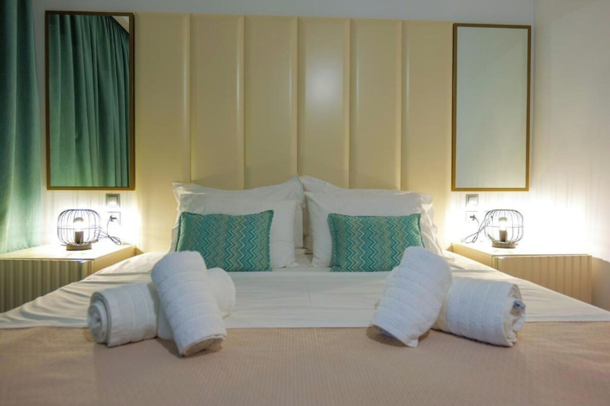 A hotel room with a large bed, two nightstands, a mirror, and a green curtain.