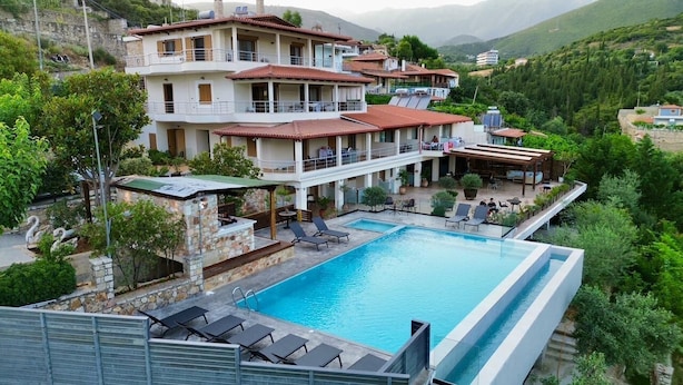 Un hotel de varios pisos con piscina, mobiliario exterior y montañas al fondo.