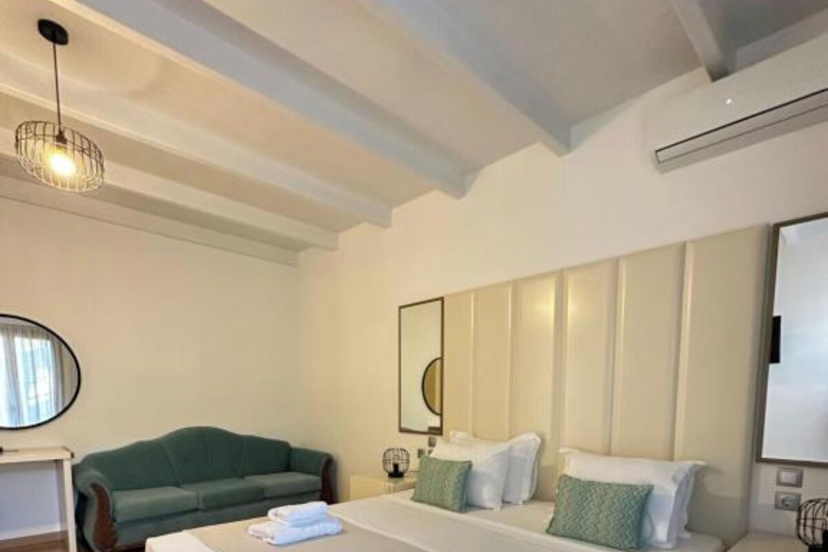 Habitación de hotel con dos camas, un sofá verde, un espejo redondo y una lámpara en el techo.
