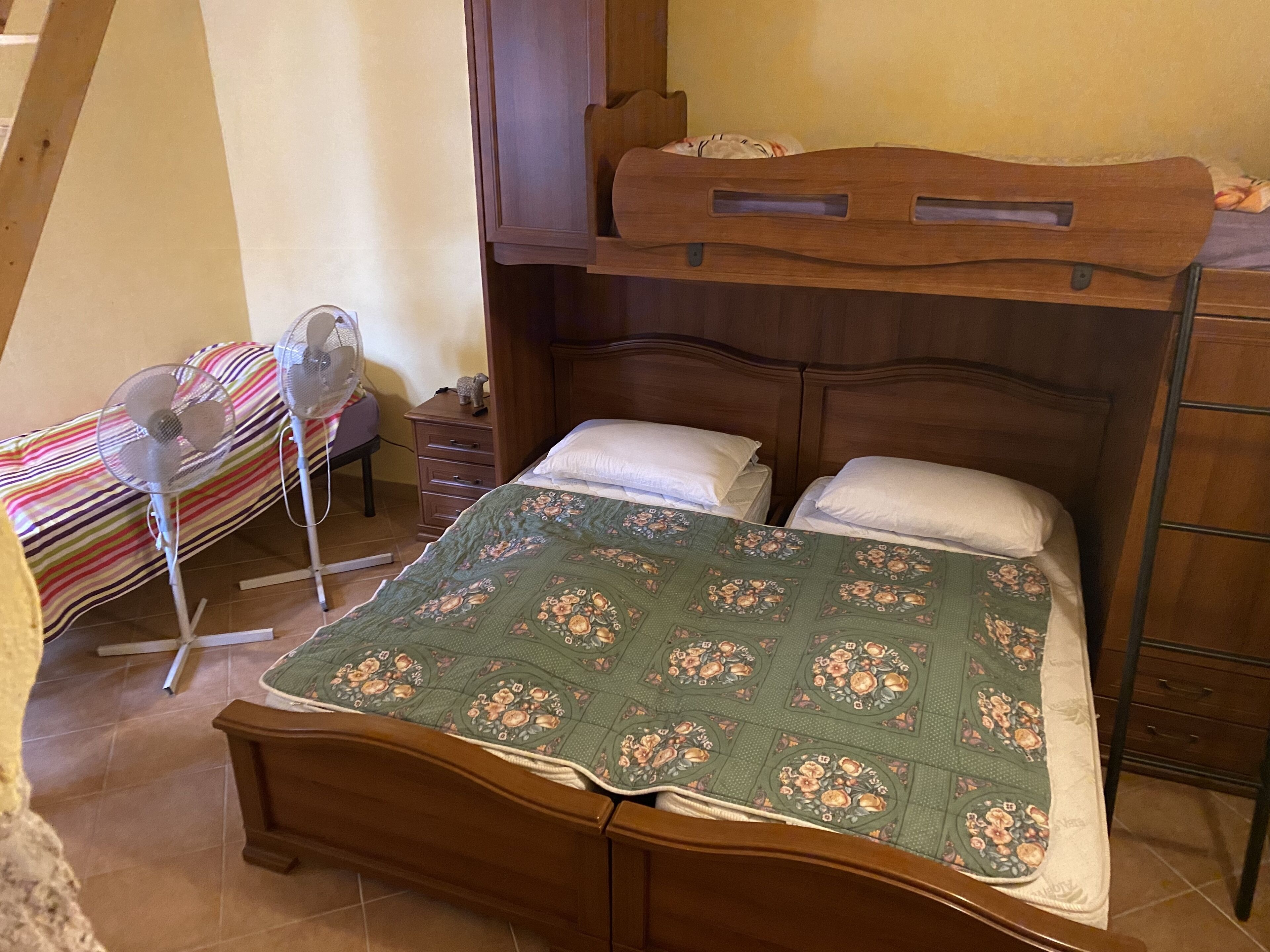Een slaapkamer met een stapelbed, een nachtkastje met een lamp, een stoel en een gestreepte deken.