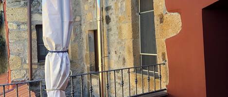 Un balcón con baranda de metal, un espacio al aire libre cubierto y un muro de piedra.
