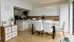 A modern kitchen with white cabinets, a dining area with white chairs, and a wooden floor. - Luxe 3 Bed property with beautiful garden room. (Harrogate)
