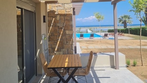 An outdoor patio with a table and chairs, a stone wall, and a view of a pool and beach. - Luxury New Loft Apartments in Halkidiki (Agios Mamas, Chalkidiki)