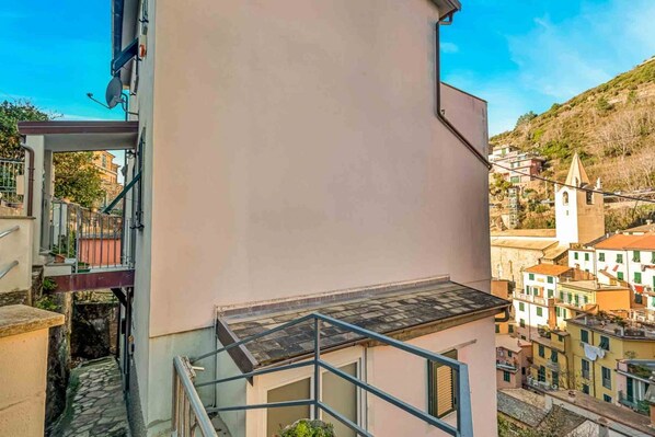 A building with a balcony, a staircase, and a view of a town with buildings and a church.