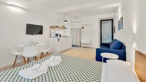 A hotel room with a bed, a TV, a dining area, a sofa, and a bathroom. - GuestHost - Riomaggiore cozy studio x4! (Riomaggiore)