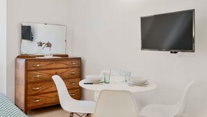 A modern room with a wooden dresser, a round dining table with chairs, a flat-screen TV mounted on the wall, and a mirror above the dresser. - GuestHost - Riomaggiore cozy studio x4! (Riomaggiore)