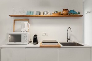 A kitchen with a microwave, kettle, coffee maker, and a sink.