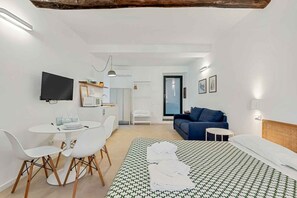 A modern hotel room with a bed, a desk with chairs, a television, and a sofa. - GuestHost - Riomaggiore cozy studio x4! (Riomaggiore)