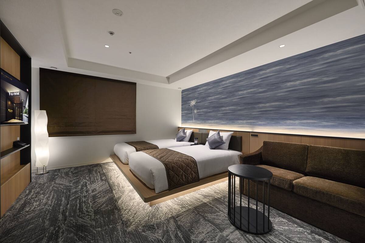 Une chambre d’hôtel moderne avec un grand lit, un canapé, une petite table et un téléviseur fixé au mur.