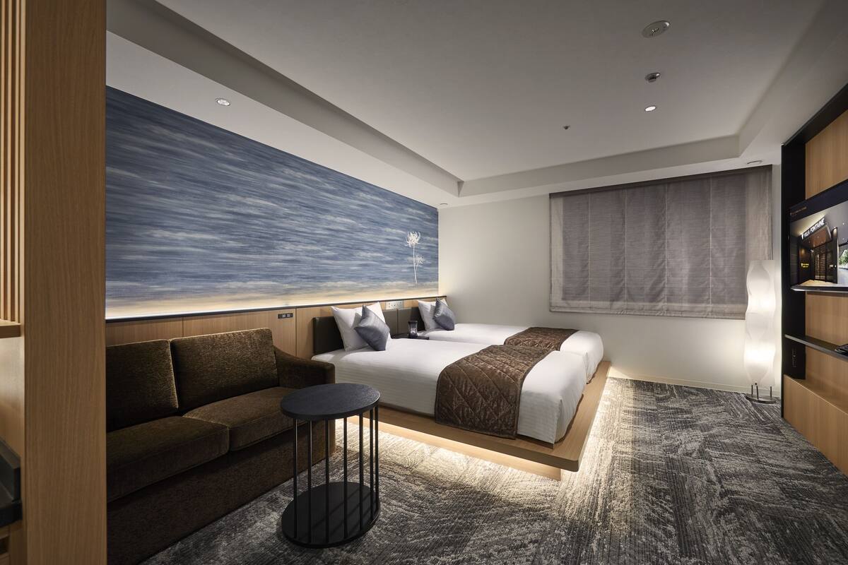 Une chambre d’hôtel moderne avec un grand lit, un canapé, une petite table ronde et un grand tableau abstrait accroché au mur.
