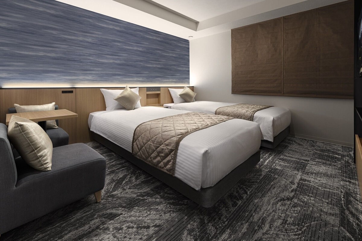 Une chambre d’hôtel avec deux lits, un canapé, une petite table et une grande fenêtre.