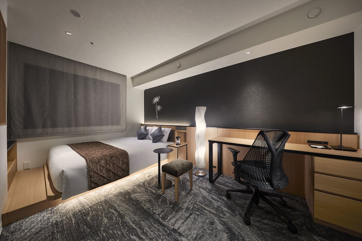 Une chambre d’hôtel moderne équipée d’un lit, d’un bureau, d’une chaise et d’une grande fenêtre avec des rideaux.