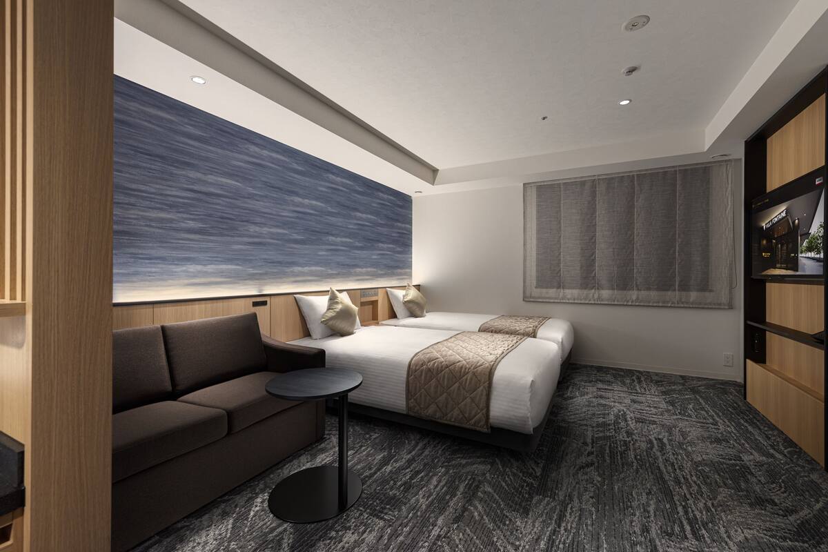 Une chambre d’hôtel moderne avec un grand lit, un canapé, une petite table ronde et un grand tableau abstrait accroché au mur.