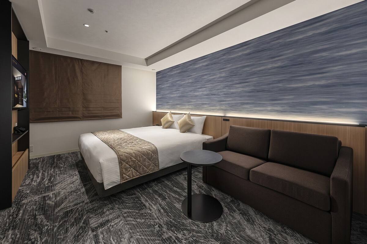 Une chambre d’hôtel moderne comprenant un lit, un canapé, une petite table et une grande œuvre d’art abstraite au mur.