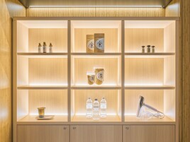 A well-lit, wooden-framed shelf unit with various items including bottles, jars, and a hairdryer.