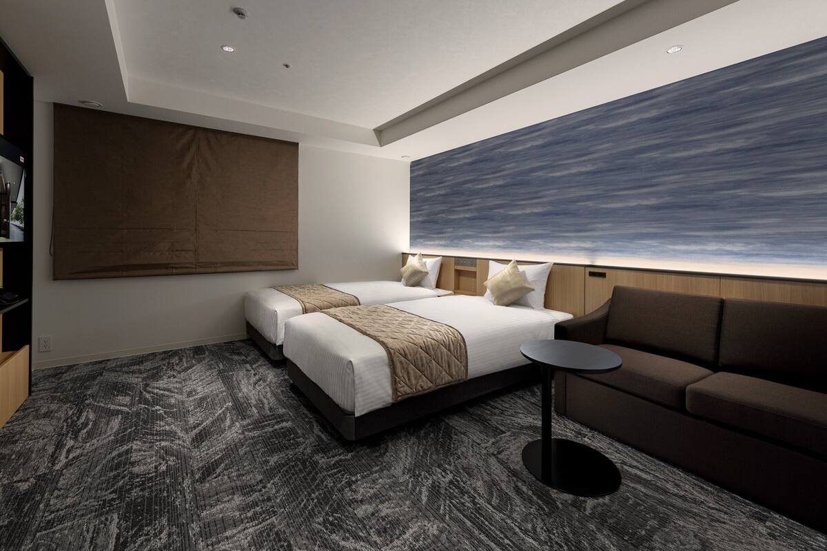 Une chambre d’hôtel moderne, dotée d’un grand lit, d’un canapé, d’une petite table et d’une grande fenêtre offrant une vue sur le ciel.