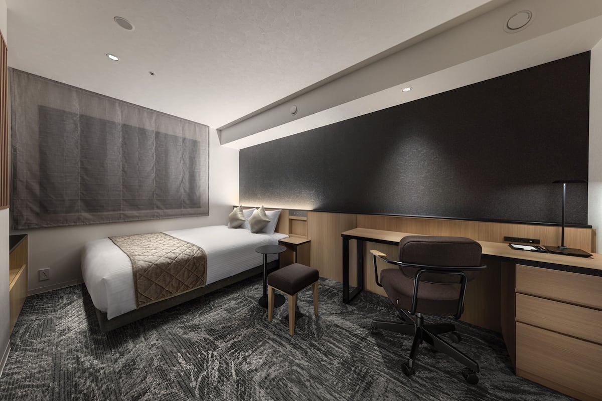 Une chambre d’hôtel moderne équipée d’un lit, d’un bureau, d’une chaise et d’une grande fenêtre avec des rideaux.