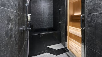 A modern bathroom with black marble tiles, a glass shower enclosure, and a wooden sauna.