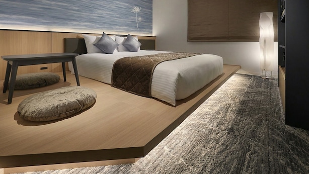 Een moderne slaapkamer met een bed, nachtkastje en een groot abstract schilderij aan de muur.