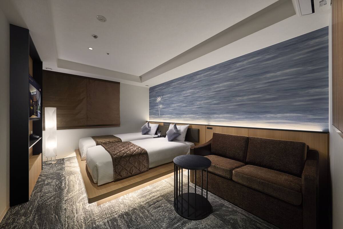 Une chambre d’hôtel moderne, dotée d’un grand lit, d’un canapé, d’une petite table ronde et d’une grande fenêtre offrant une vue dégagée.