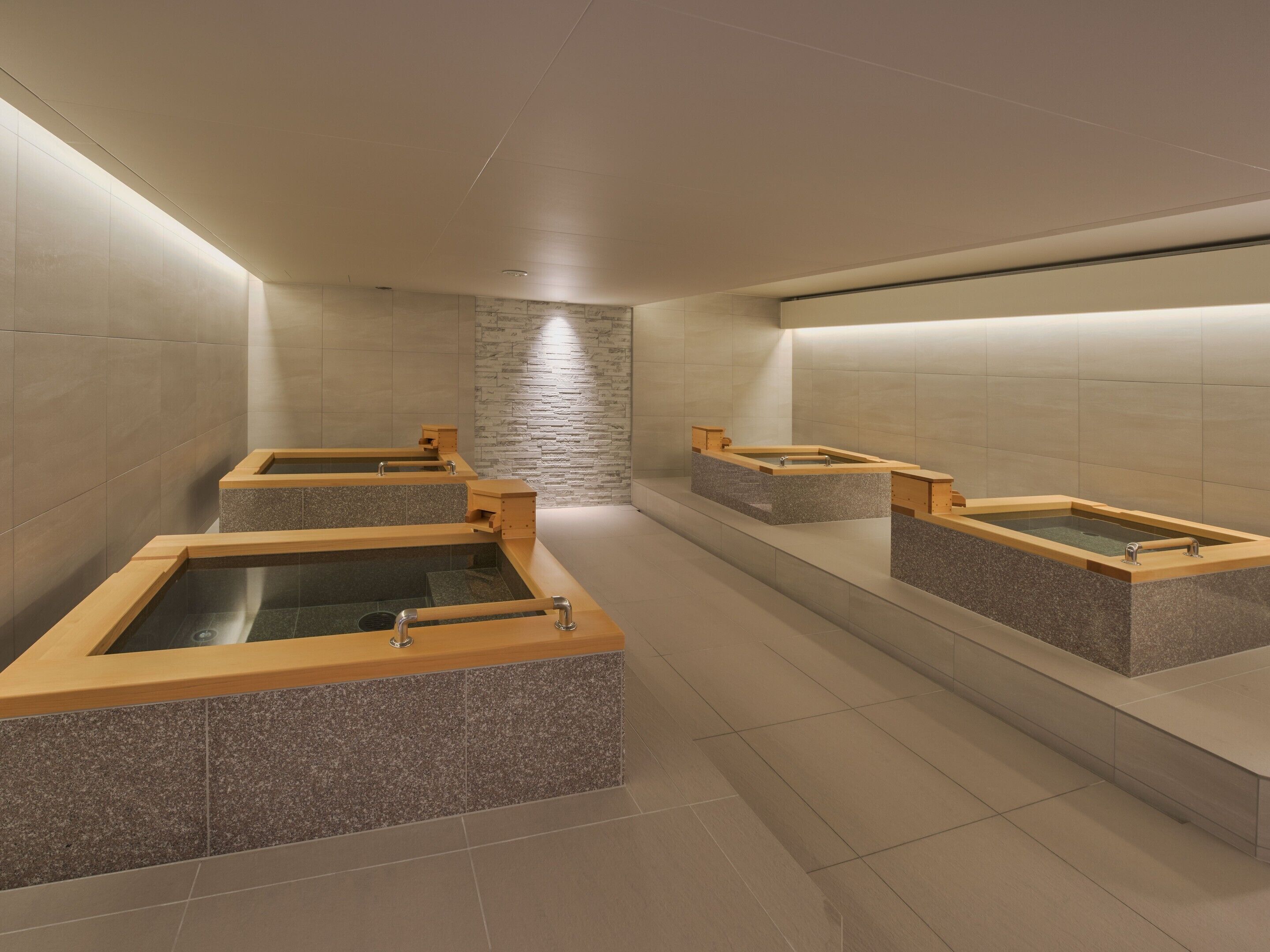 Ein moderner Wellnessbereich mit mehreren Whirlpools und einer Steinwand.