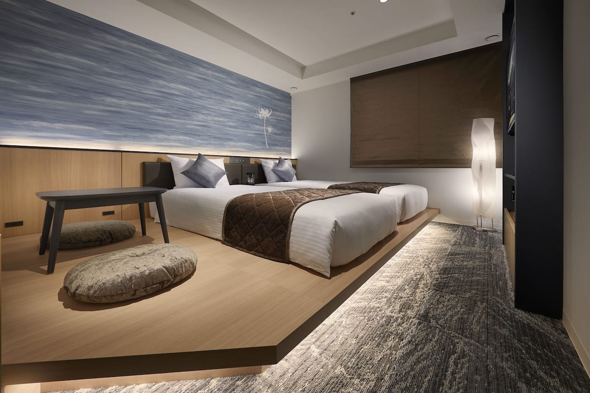 Une chambre moderne avec un grand lit, des tables de chevet, une petite table et une lampe fixée au mur.