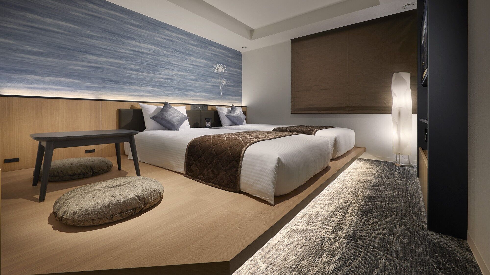 A modern hotel room with a large bed, a desk, a chair, and a large window.