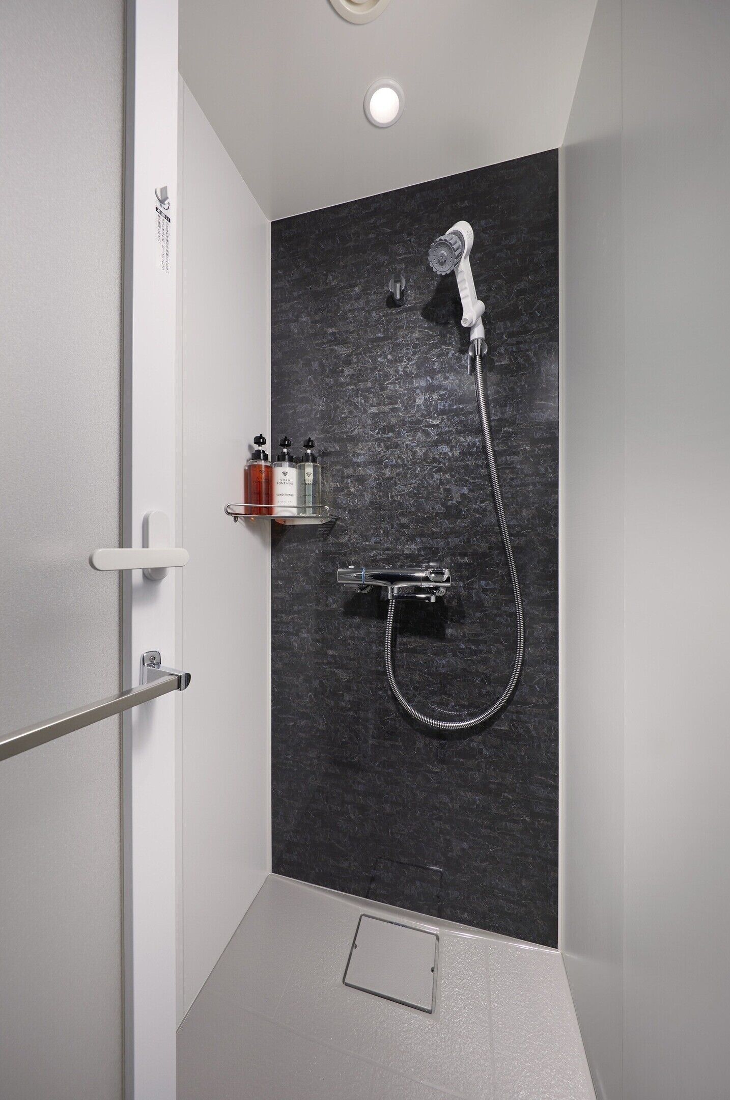 Et moderne brusebad med brusehoved, vægmonteret armatur og hylde med toiletartikler.