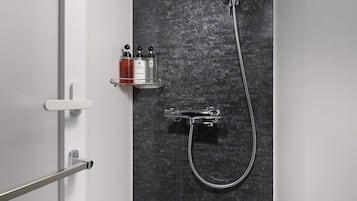 Et moderne brusebad med brusehoved, vægmonteret armatur og hylde med toiletartikler.