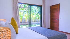Een slaapkamer met een bed, een raam met uitzicht op groen, en een houten deur.