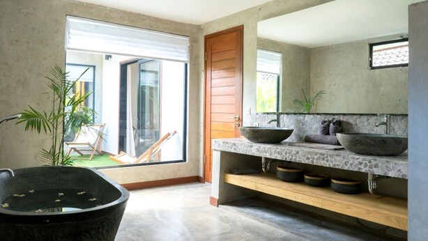 Een moderne badkamer met een groot stenen wastafel, een houten deur en uitzicht op buiten.
