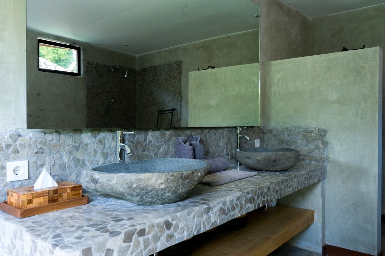 Ein Badezimmer mit einer Steintafel, zwei großen Steinswaschbecken, einer Holzschatulle mit Taschentüchern und einem kleinen Fenster.