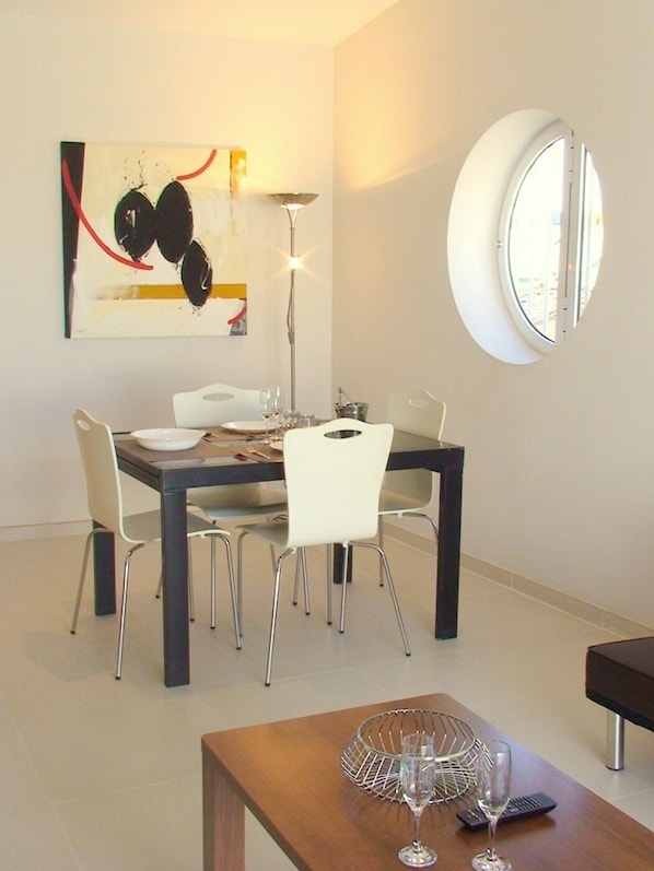 Uma sala de jantar moderna com uma mesa redonda, cadeiras brancas e uma pintura contemporânea na parede.