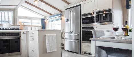 Una cocina moderna con horno empotrado, un refrigerador grande y un comedor con una mesa para dos.