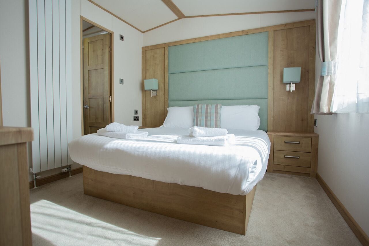 Un letto rifatto con lenzuola e asciugamani bianchi, una testiera in legno, lampade da comodino e un comodino in legno con cassetti.