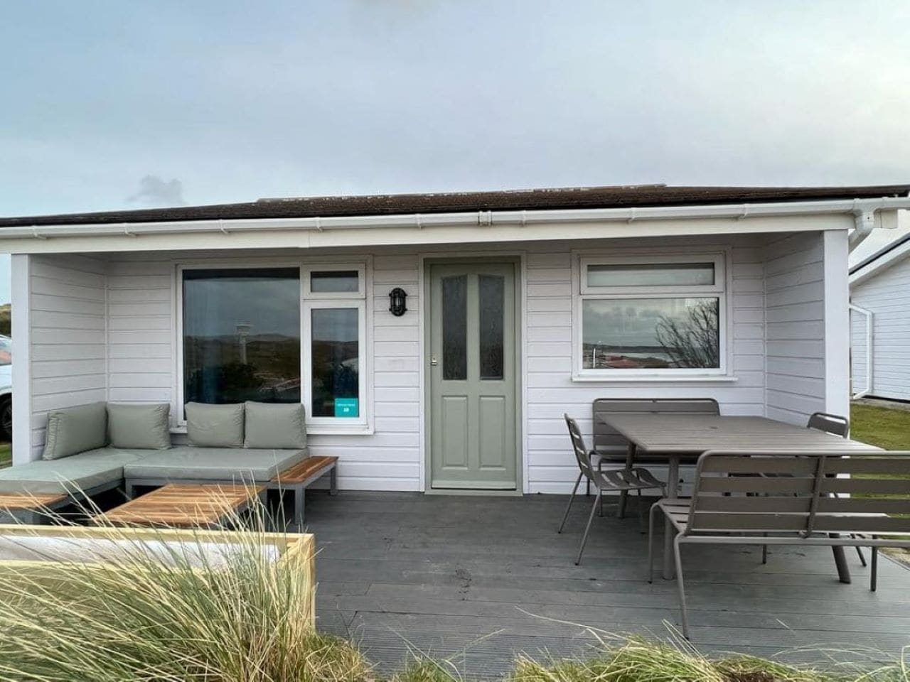 A single-story house with a front porch, a sliding glass door, a green door, and a patio area with a table and chairs.