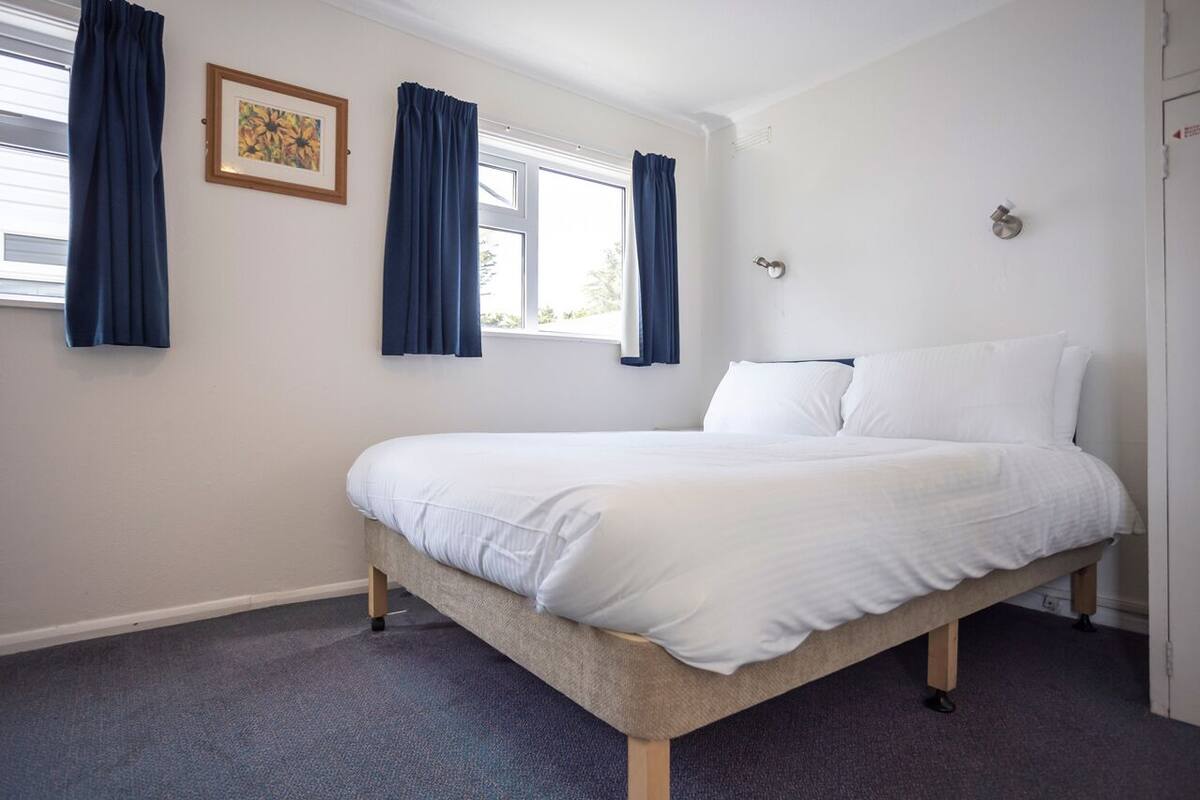A bedroom with a bed, curtains, a framed picture, and a window.