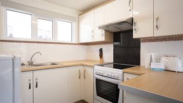 A compact kitchen with white cabinets, a stove, a sink, and a window above the countertop.
