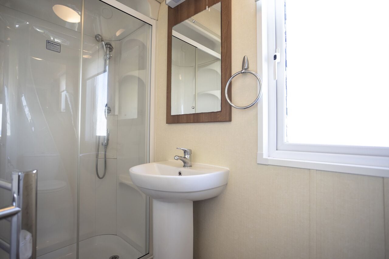 Ein modernes Badezimmer mit einer gläsernen Duschkabine, einem weißen Waschbecken und einem Spiegel mit Holzrahmen.