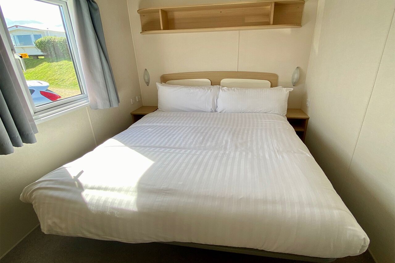A neatly made bed with white linens, a wooden headboard, and a window with curtains.
