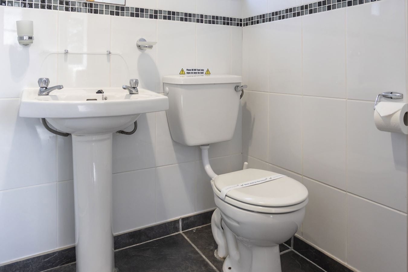 A bathroom with a white sink, toilet, and a caution sign on the wall.