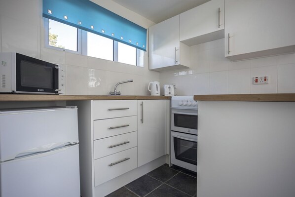 A compact kitchen with white cabinets, a microwave, a kettle, and a built-in oven. - St Ives Bay Beach Resort by Away Resorts (Hayle)